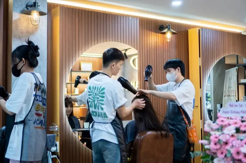 Một stylist đang nhuộm tóc cho khách hàng trong không gian sạch sẽ của một quán tóc gần đây, tập trung vào quá trình làm việc chuyên nghiệp.