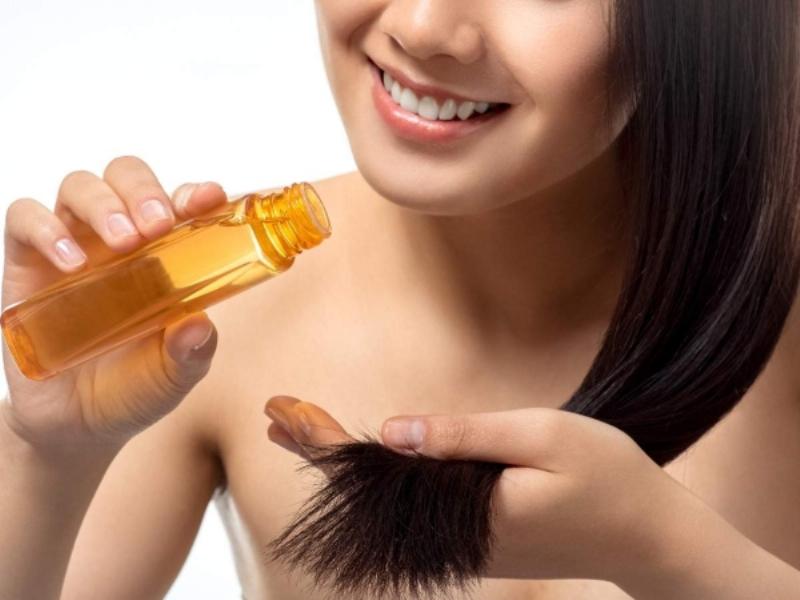 Một người đang bôi serum dưỡng tóc lên mái tóc khô sau khi gội, minh họa bước chăm sóc tóc tại nhà sau khi làm dịch vụ tại salon.