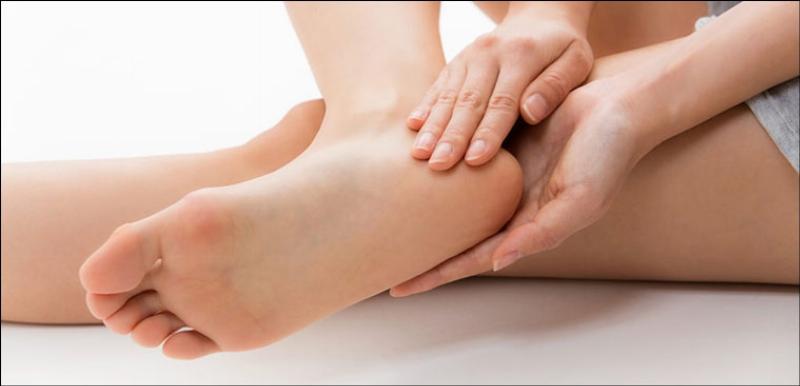 Một người đang sử dụng đá bọt để tẩy tế bào chết vùng da dày ở gót chân, minh họa cách xử lý các vùng da chai sần.